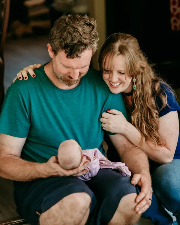 New parents sitting in their doorway holding their newborn daughter
