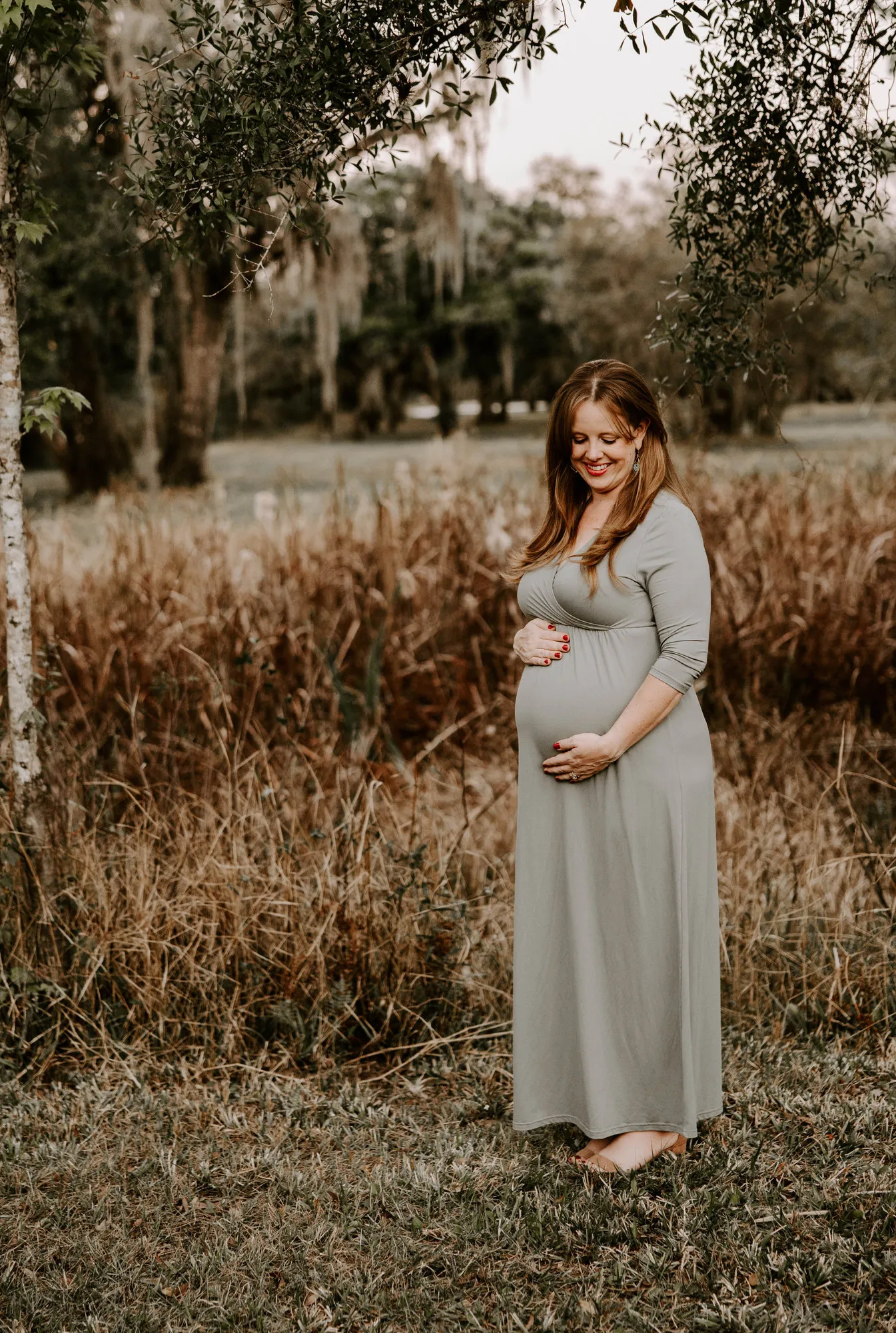 Expectant mother looking down at her bump beside a young tree
