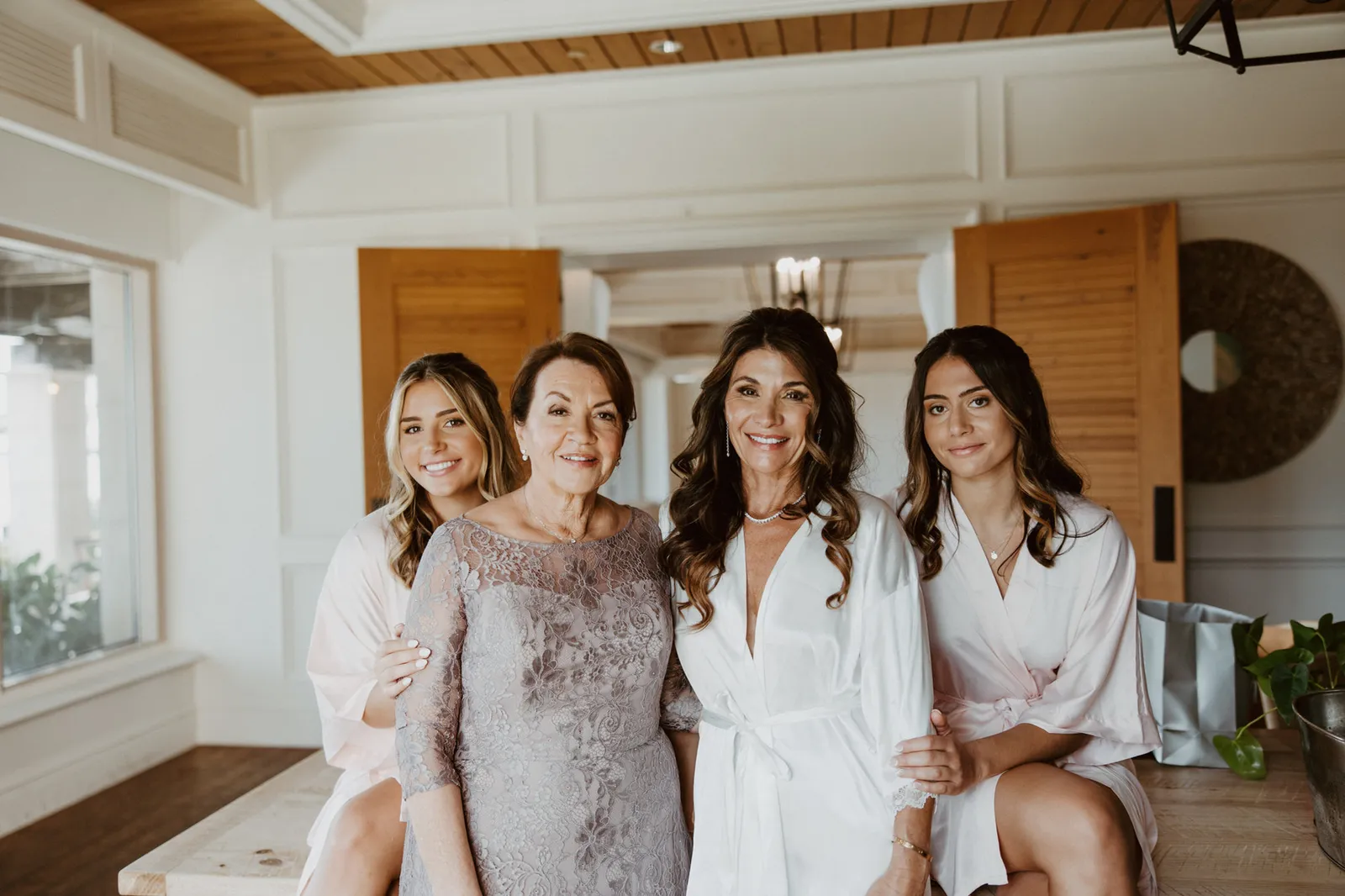 Bride in a white robe with two bridesmaids and a woman in a lilac lace dress