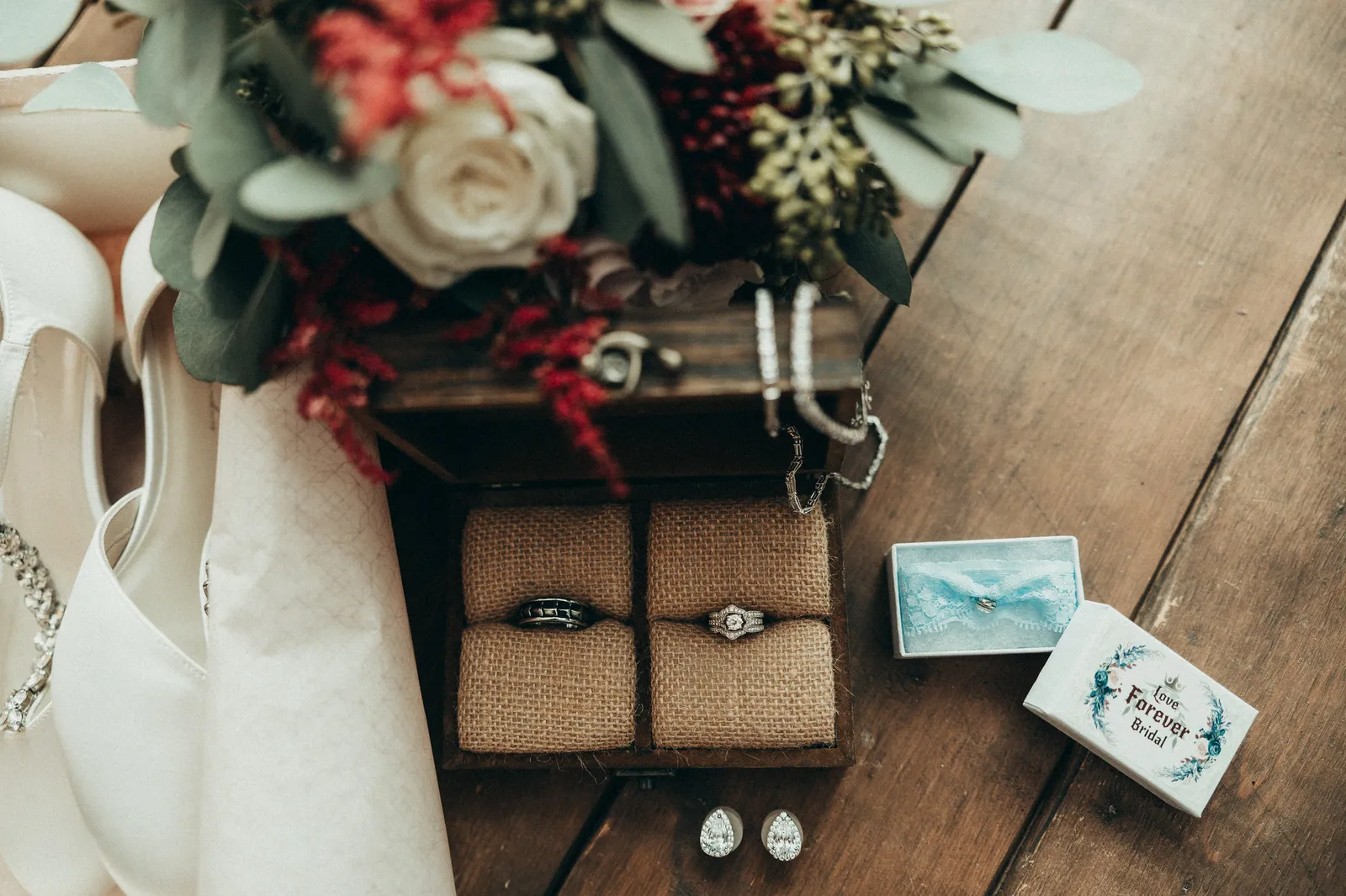 Wedding rings in a burlap-lined box beside the bouquet and shoes