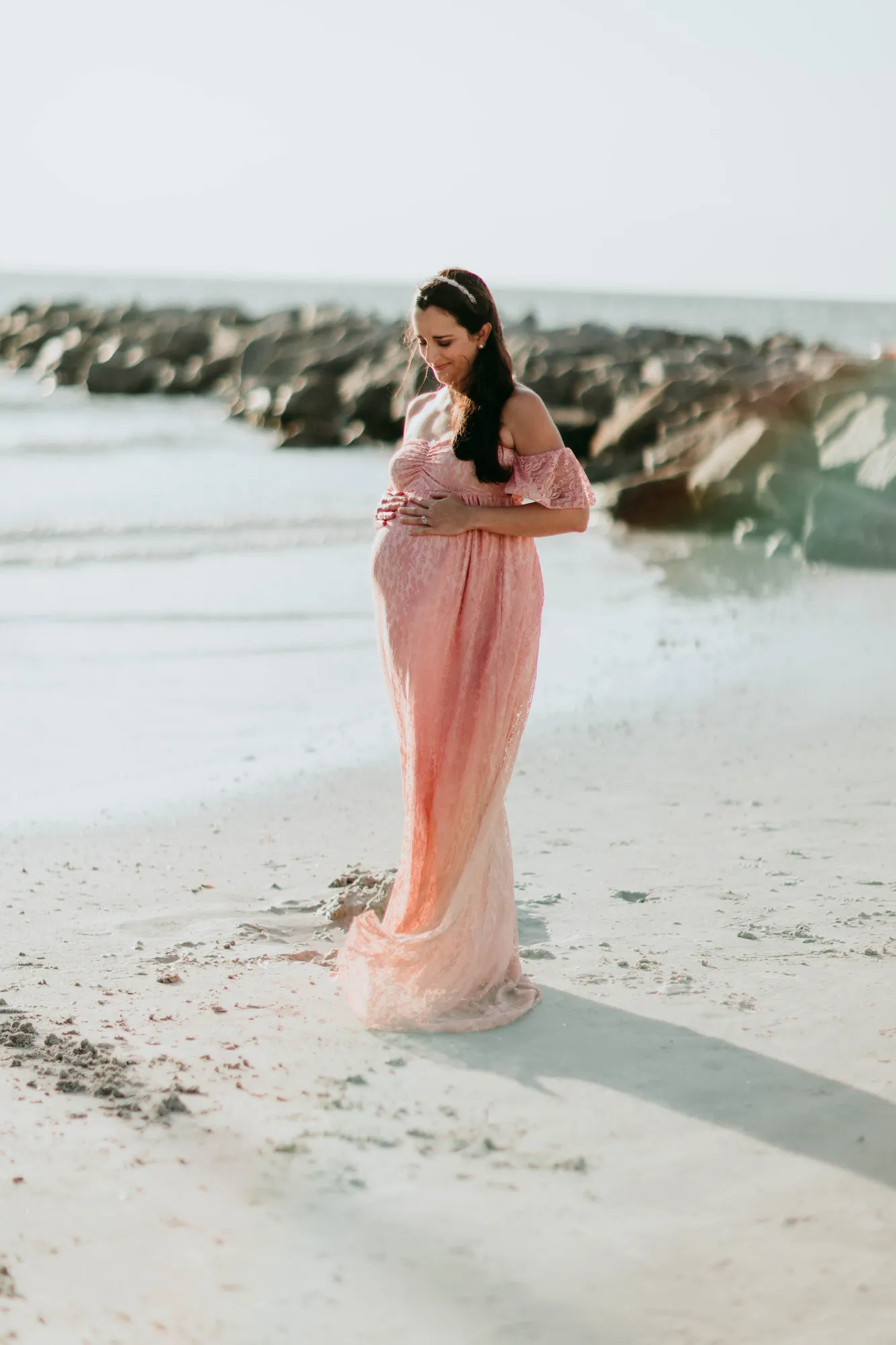 Expectant mother looking down at her bump, the rock jetty behind her