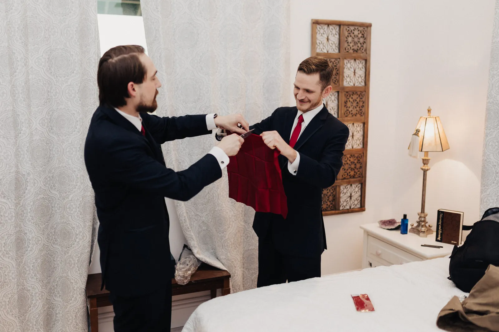 Two men in suits laughing as they hold up a small red garment
