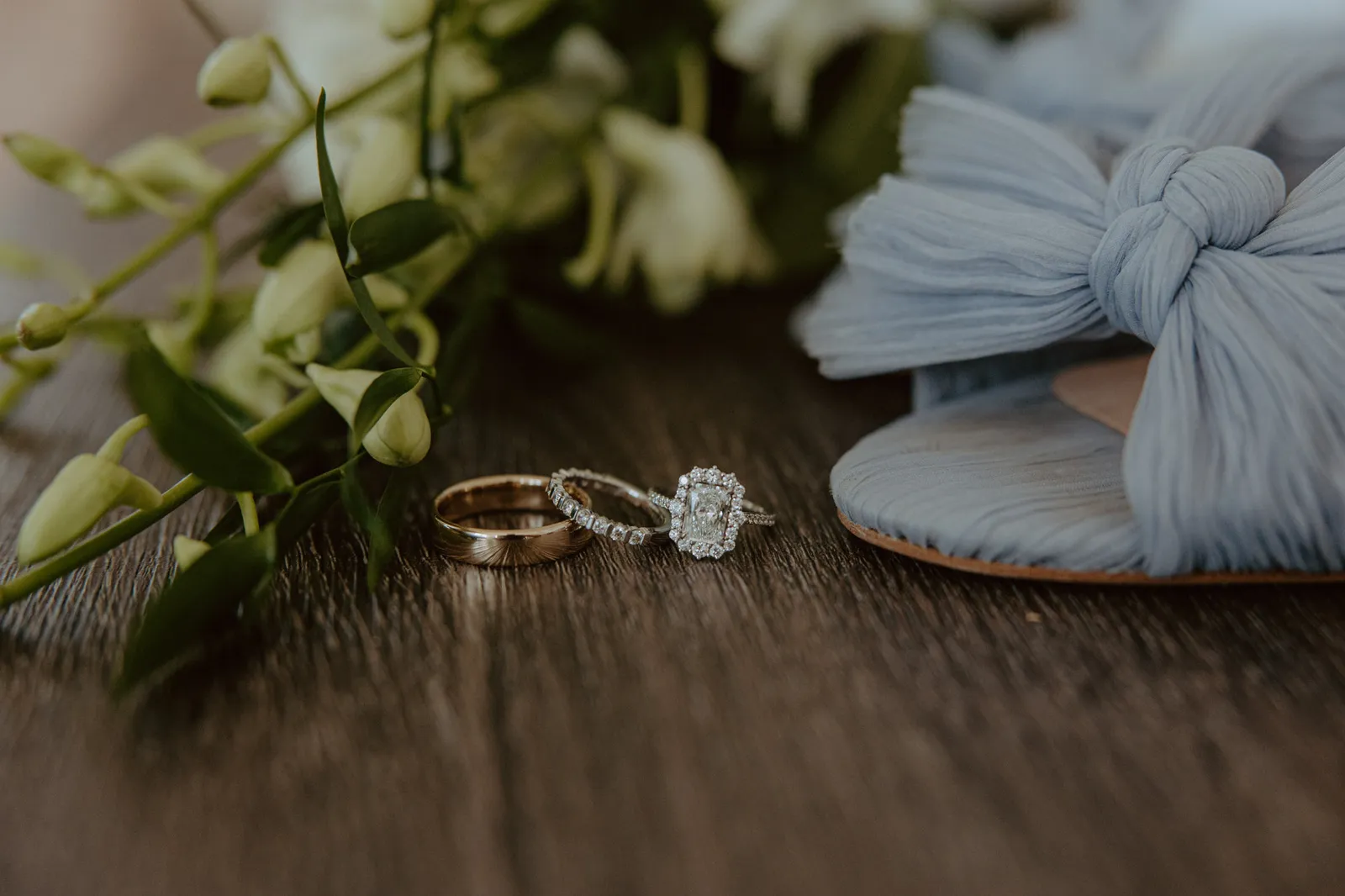 Wedding rings beside a blue bow shoe and orchids