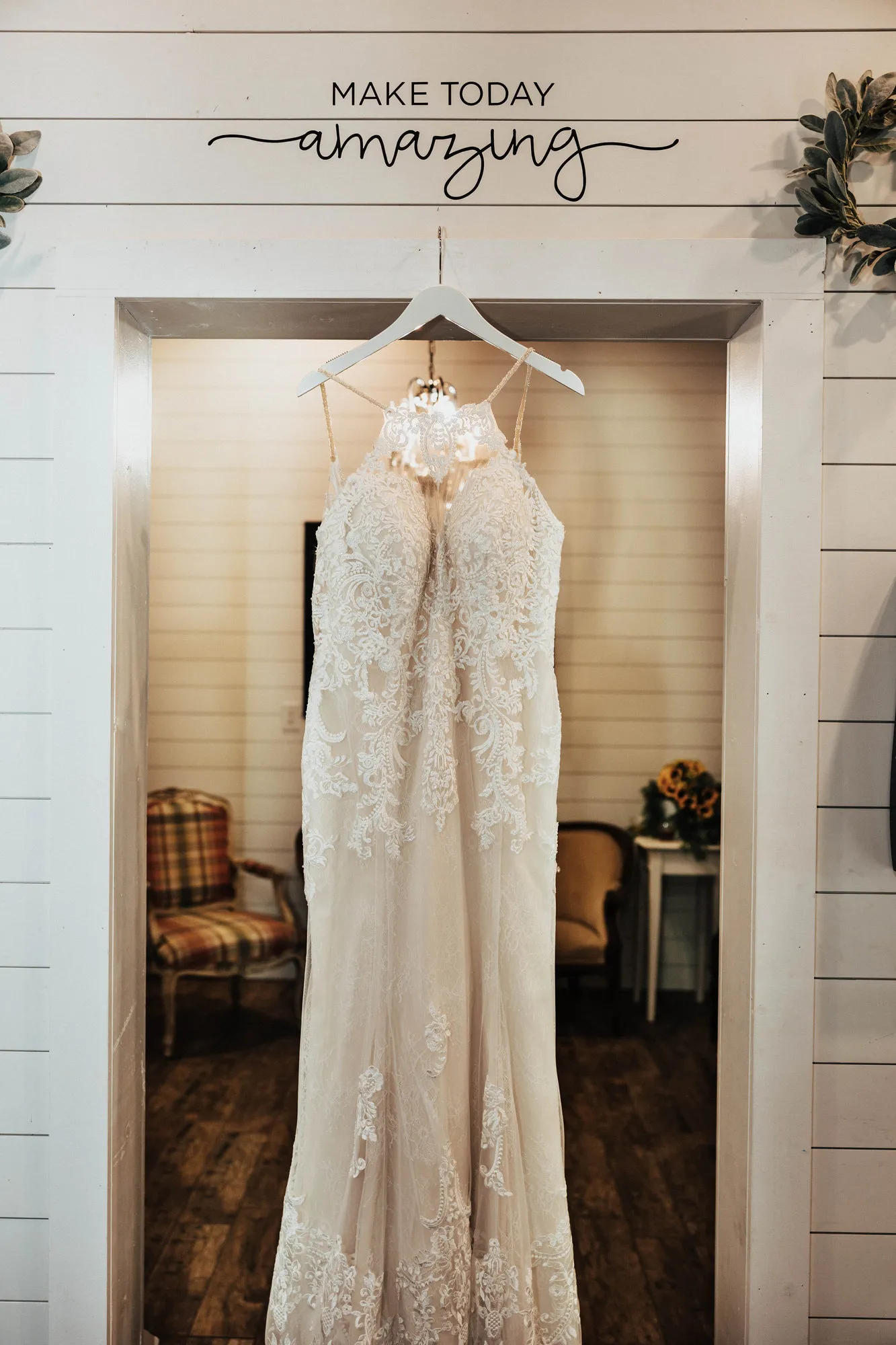 Lace wedding dress hanging in a doorway under a sign that reads Make today amazing