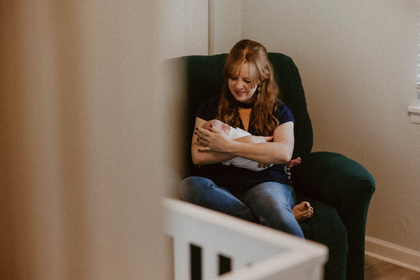 Mother cradling her newborn in an armchair, seen from the nursery doorway