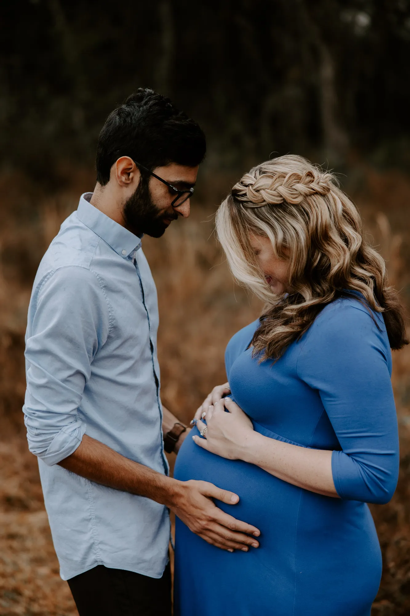 Couple standing in the field, both looking down at her bump