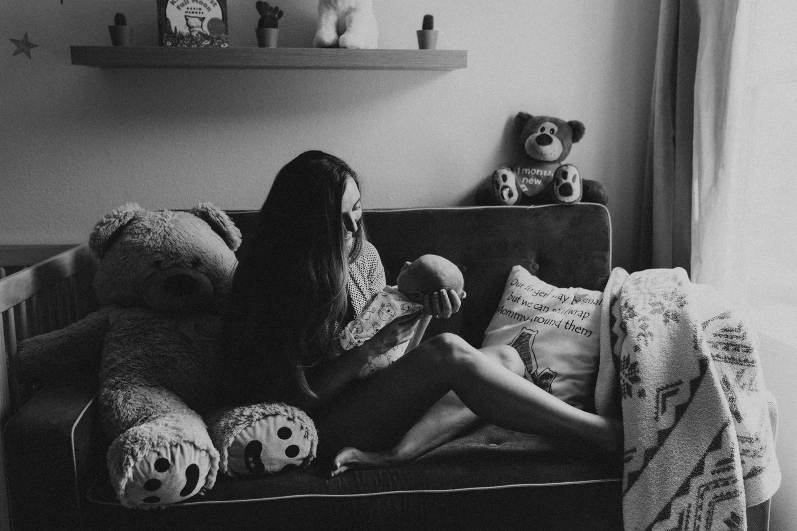 Mother feeding her newborn on a couch among teddy bears, in black and white
