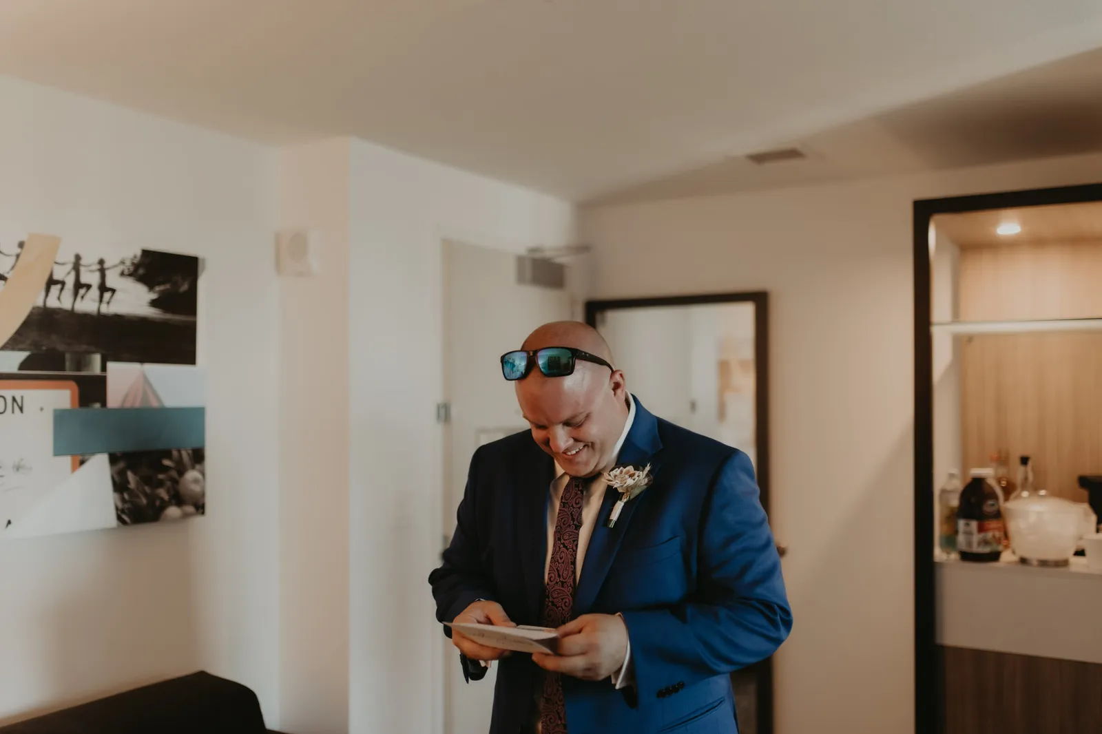Man in a blue suit and boutonniere smiling as he reads a card