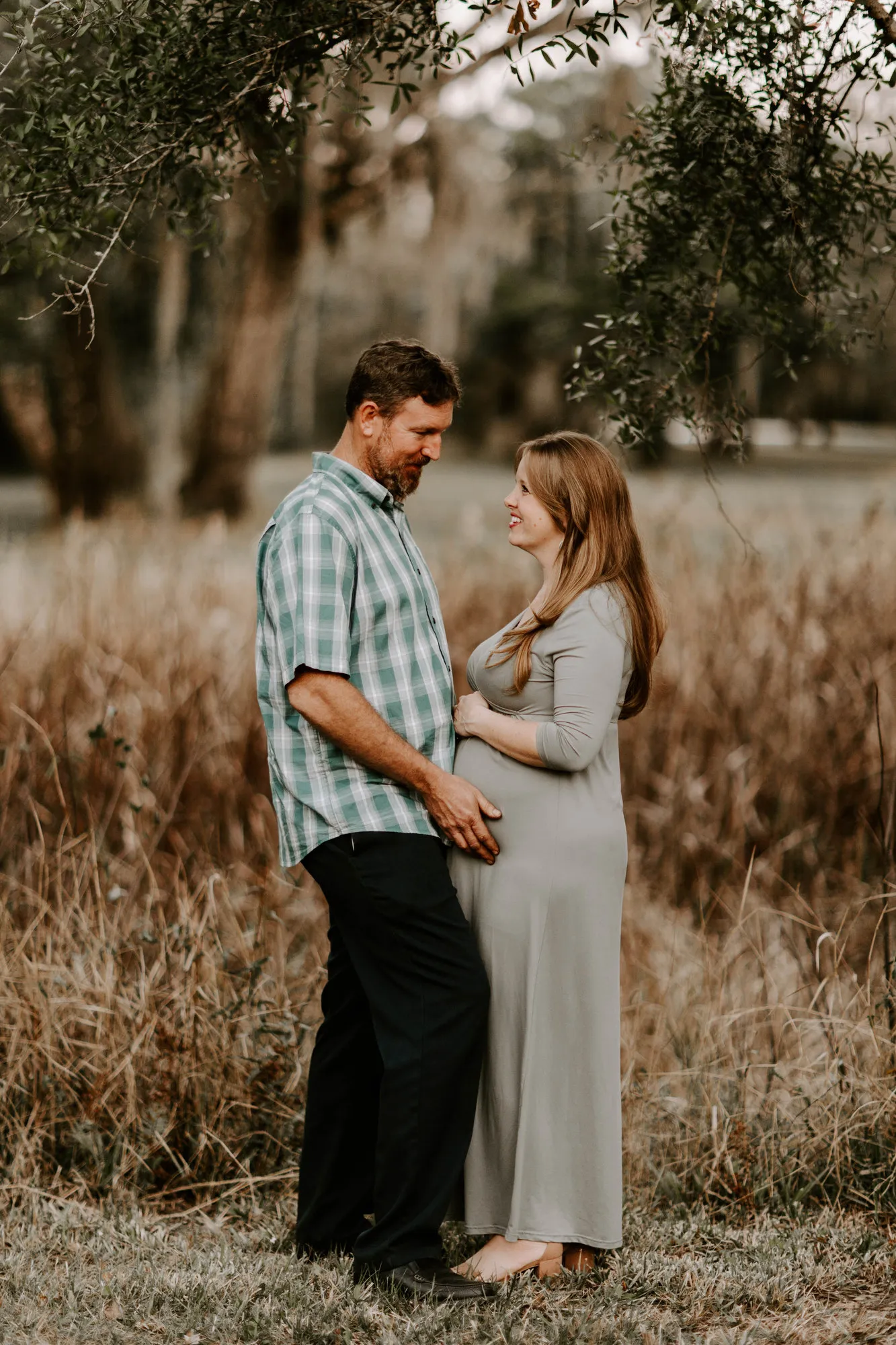 Couple laughing together in the tall grass, his hand on her bump