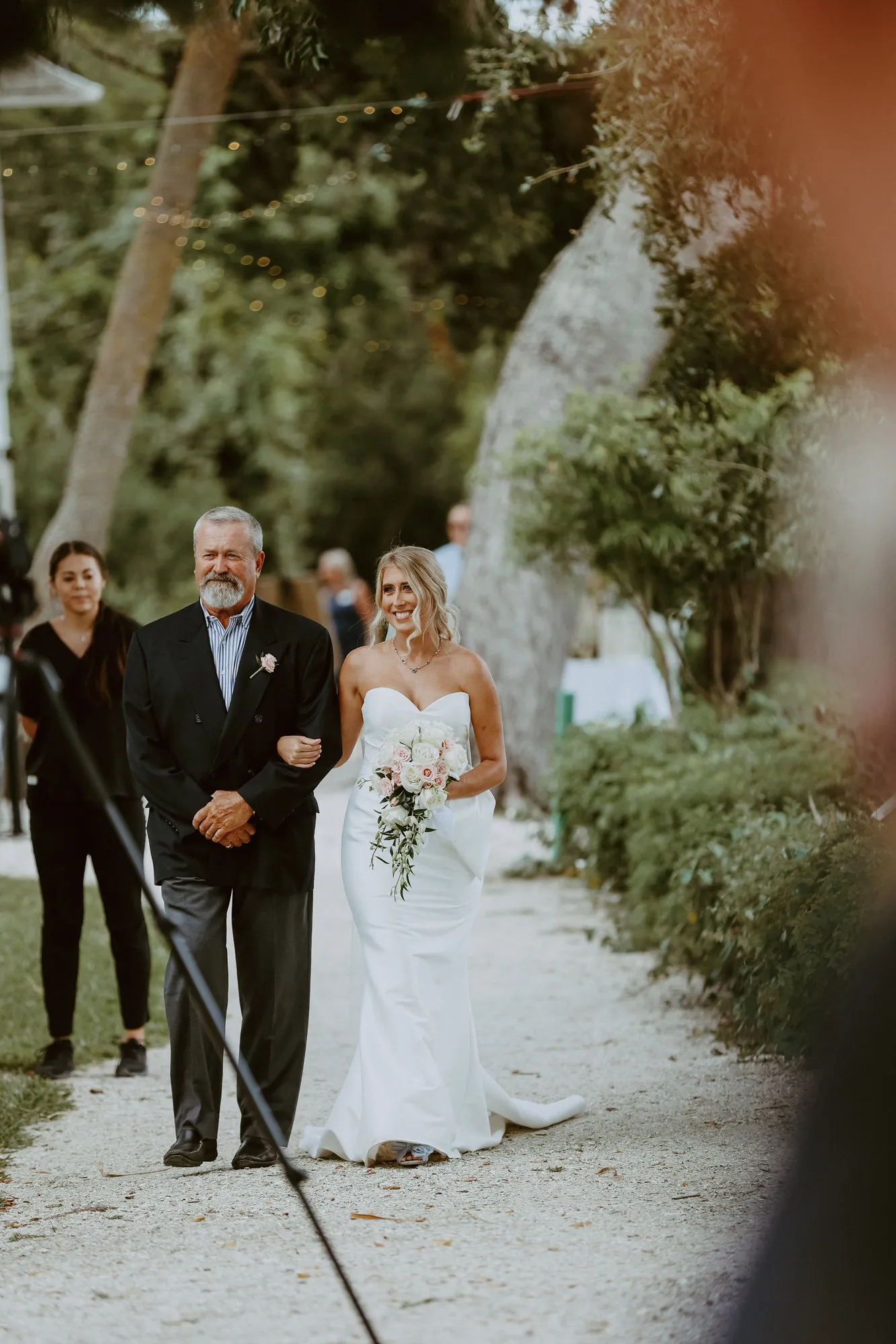 Bride walking up a shell path on the arm of a man in a dark suit