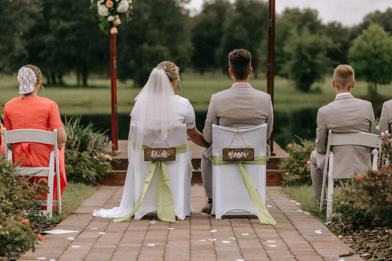 Bride and groom seated in chairs labelled bride and groom, seen from behind