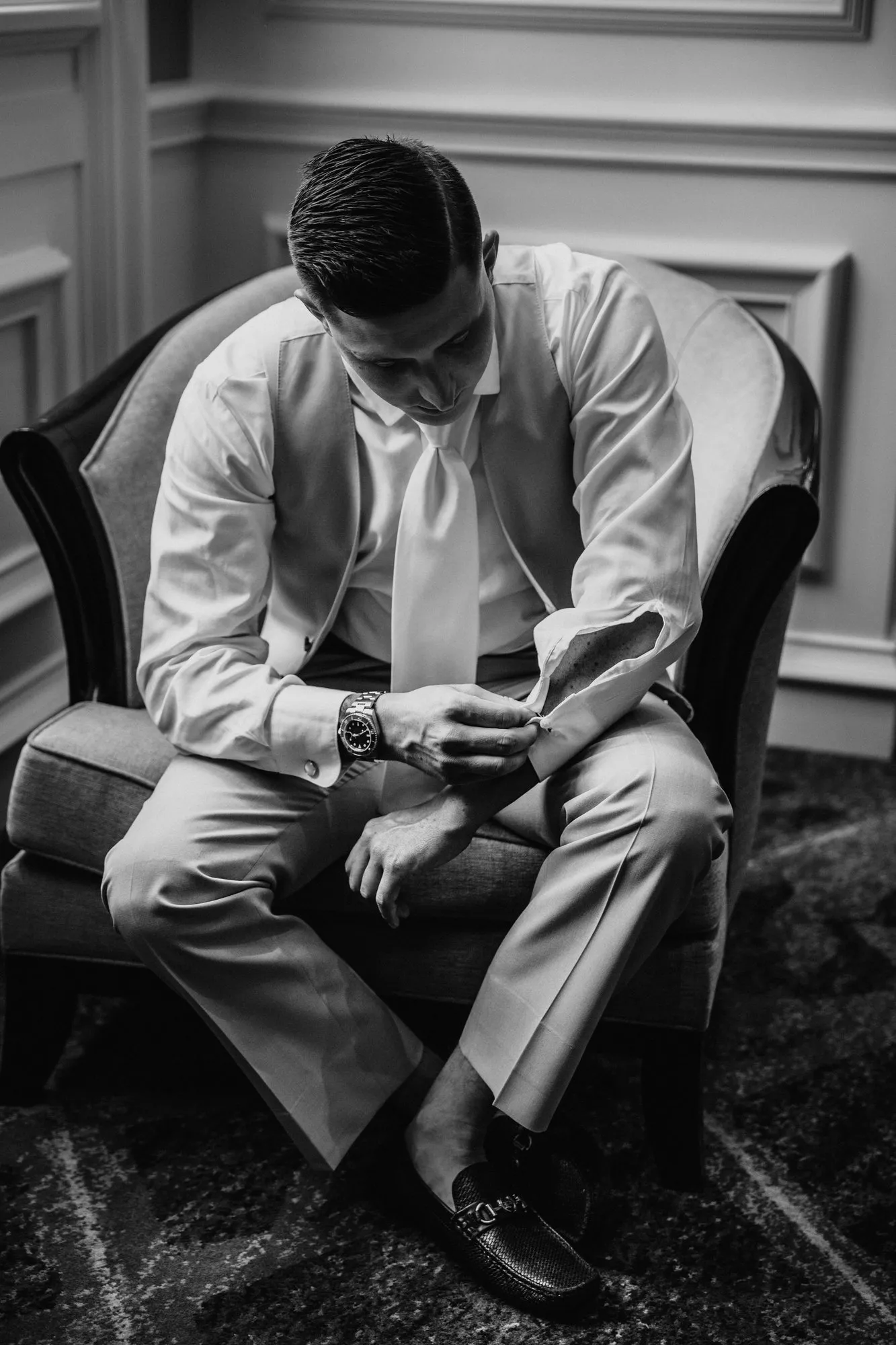 Groom seated in an armchair reading a note, in black and white