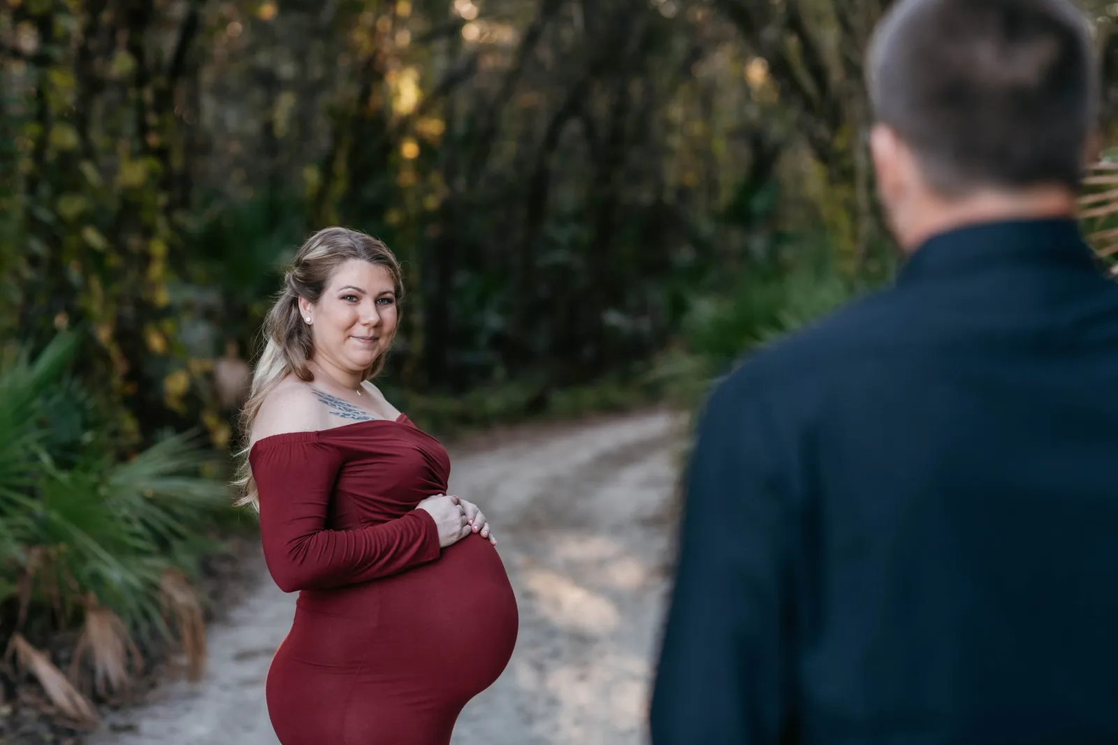 Expectant mother holding her bump on a sandy track, seen past her partner's shoulder