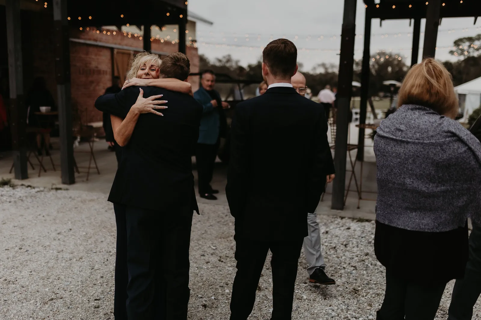 Guests in dark coats greeting each other with a hug outdoors