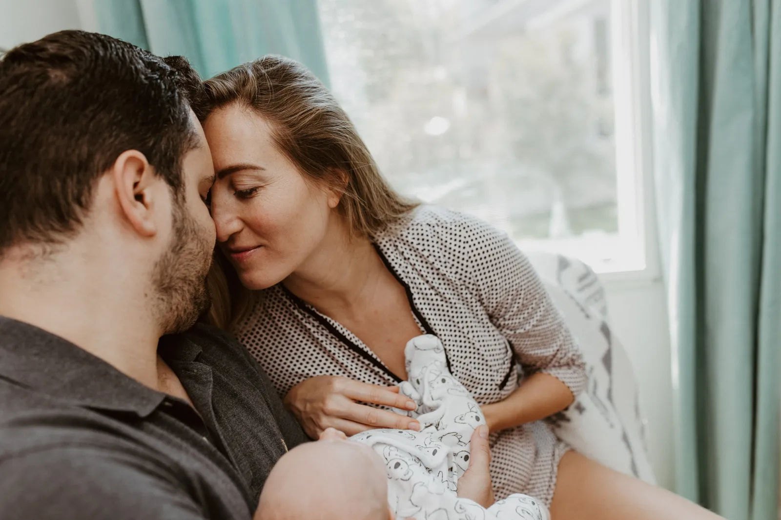Parents nose to nose with their newborn in her lap