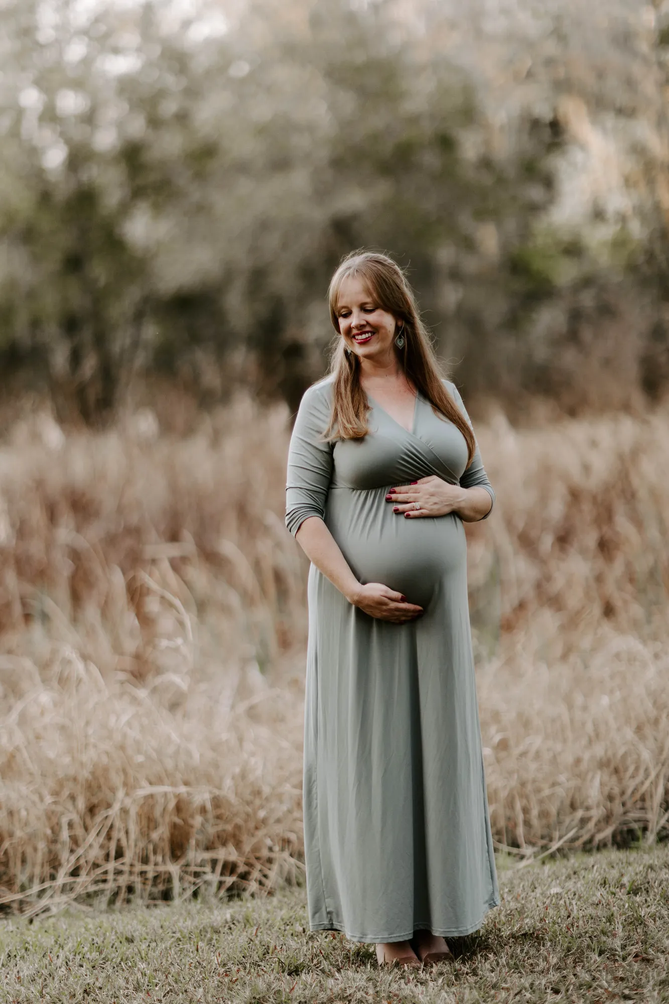 Expectant mother cradling her bump, looking down, full length