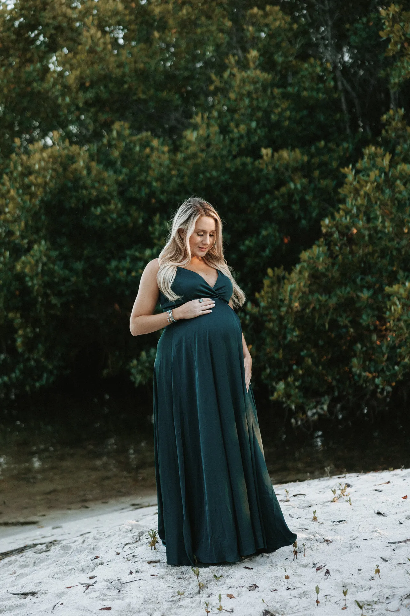 Expectant mother in an emerald gown standing in front of mangroves