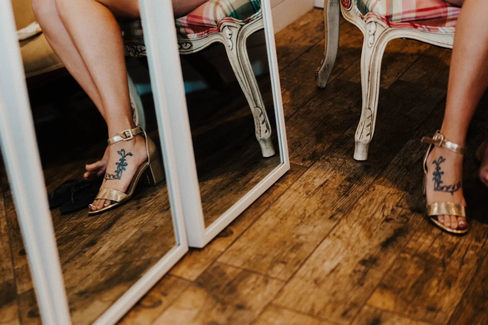 Gold heeled sandals and a tattooed foot beside floor mirrors