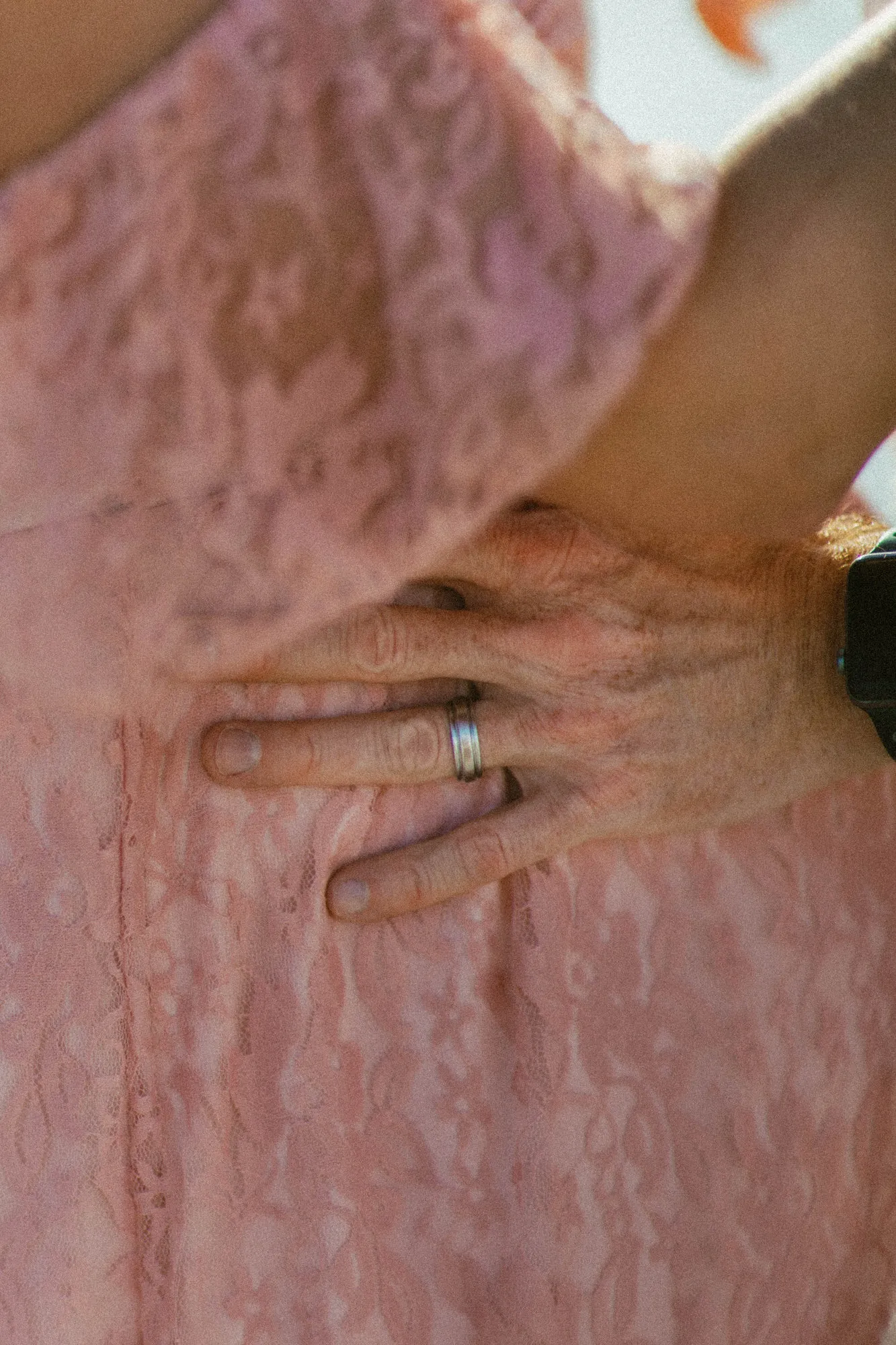 Close-up of a hand with a wedding band resting on pink lace