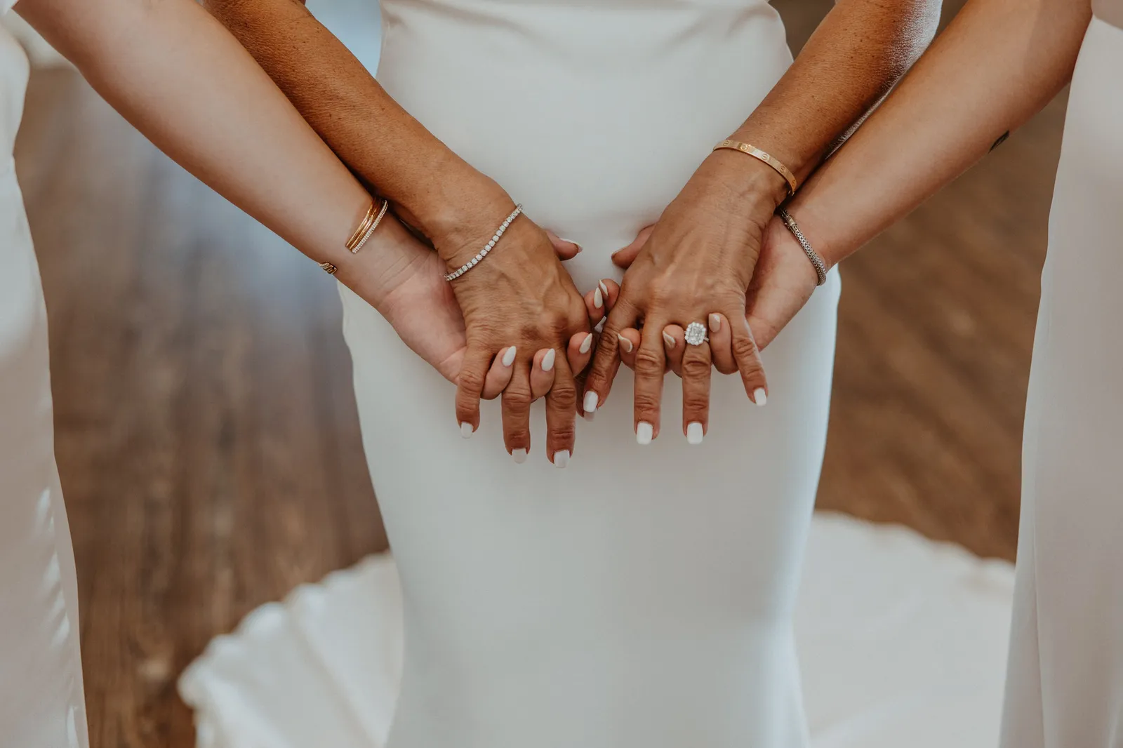 Hands with bracelets and a diamond ring layered together against the bride's white gown