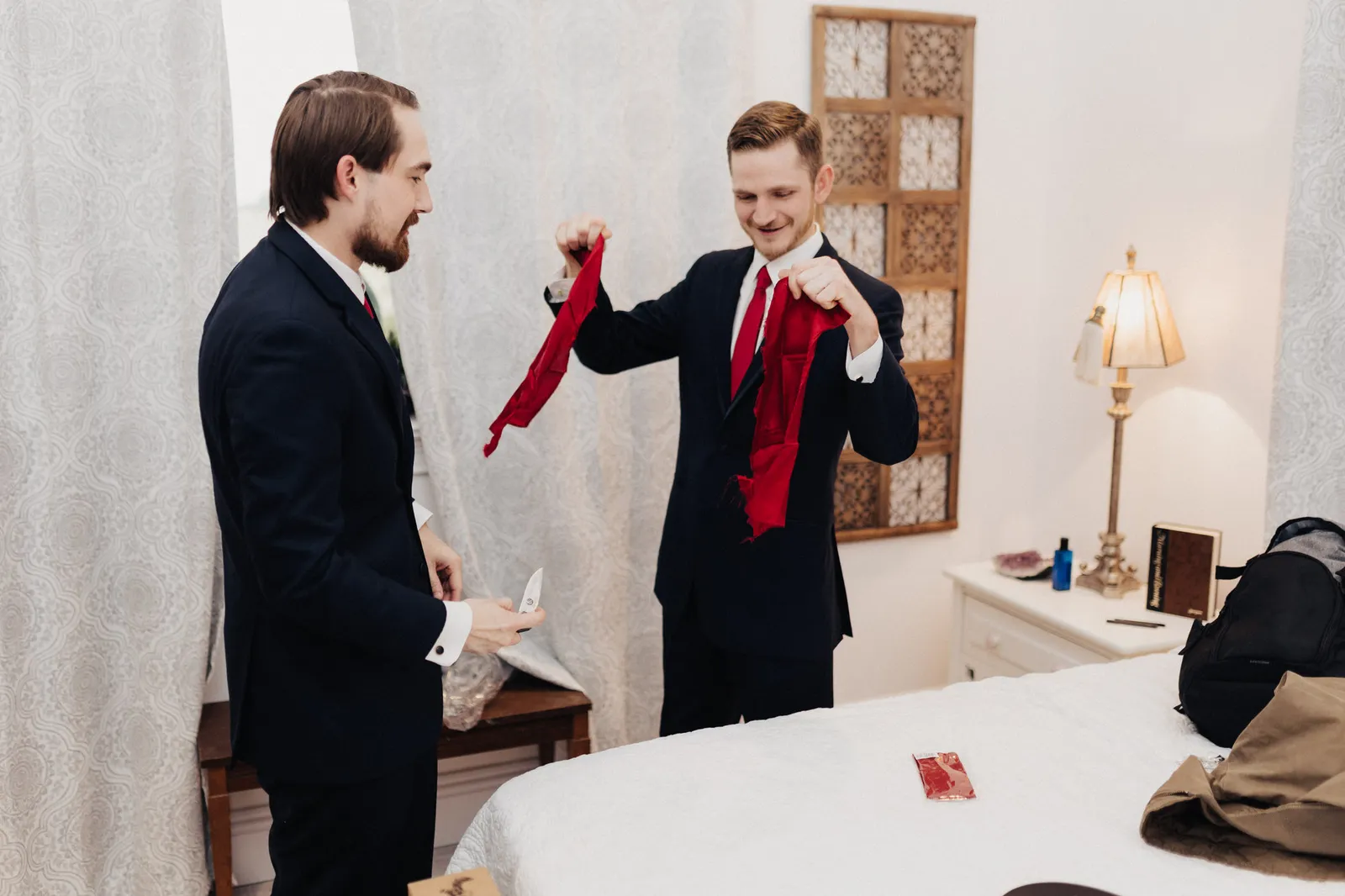 Man in a red tie laughing as he holds up a gift in each hand