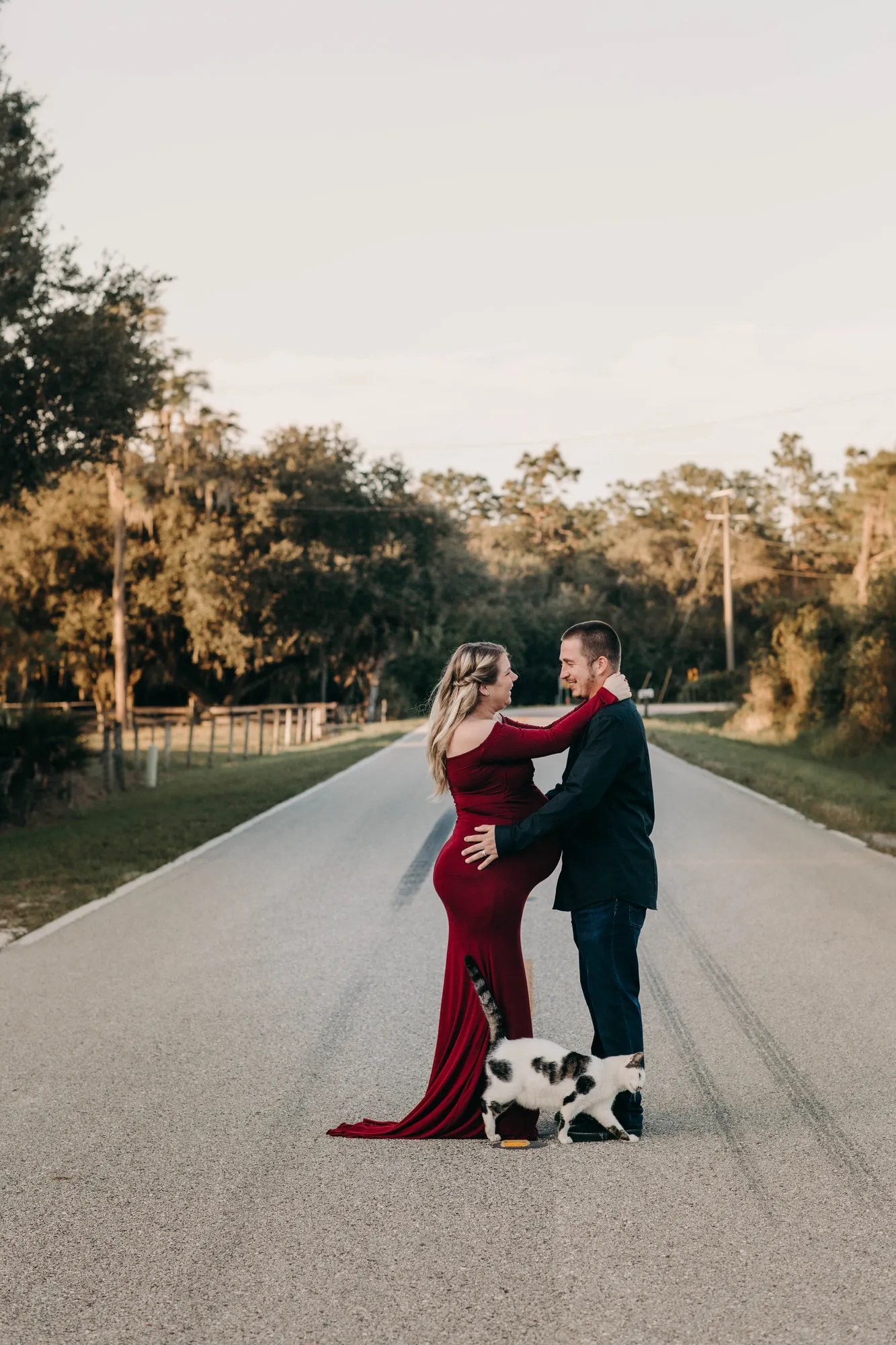 Couple embracing on a country road with a black and white dog at their feet