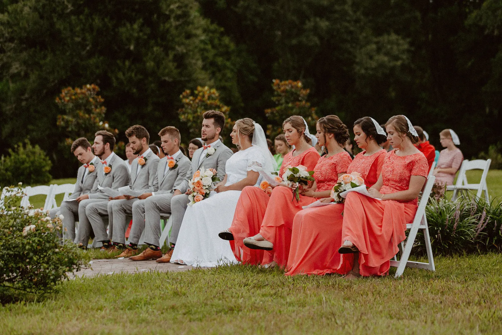 Wedding party seated in a row on the lawn, bridesmaids in coral dresses