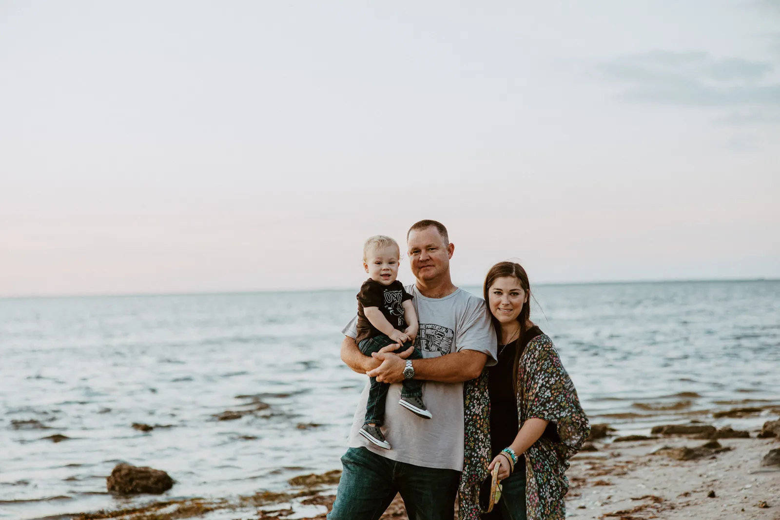 Family of three standing on the shore with the bay behind them