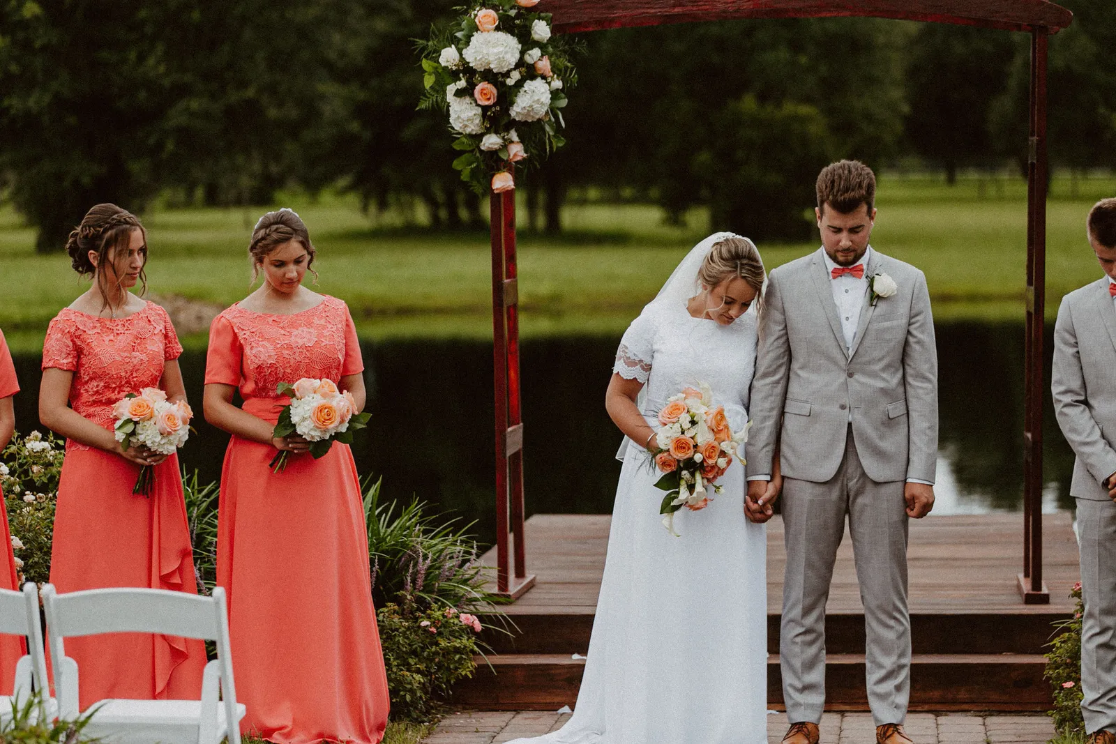 Bride and groom praying together at the ceremony arch beside a pond