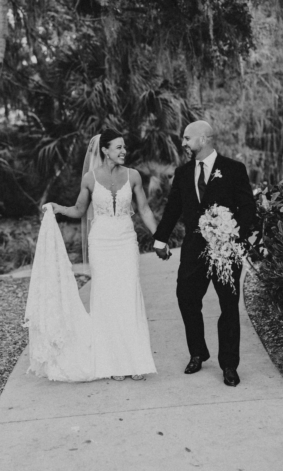 Bride and groom walking hand in hand along a garden path, in black and white