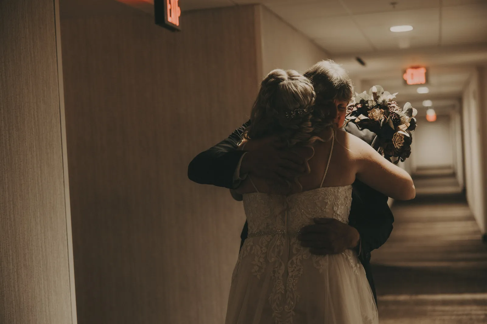 Bride hugging someone in a hotel corridor, seen from behind