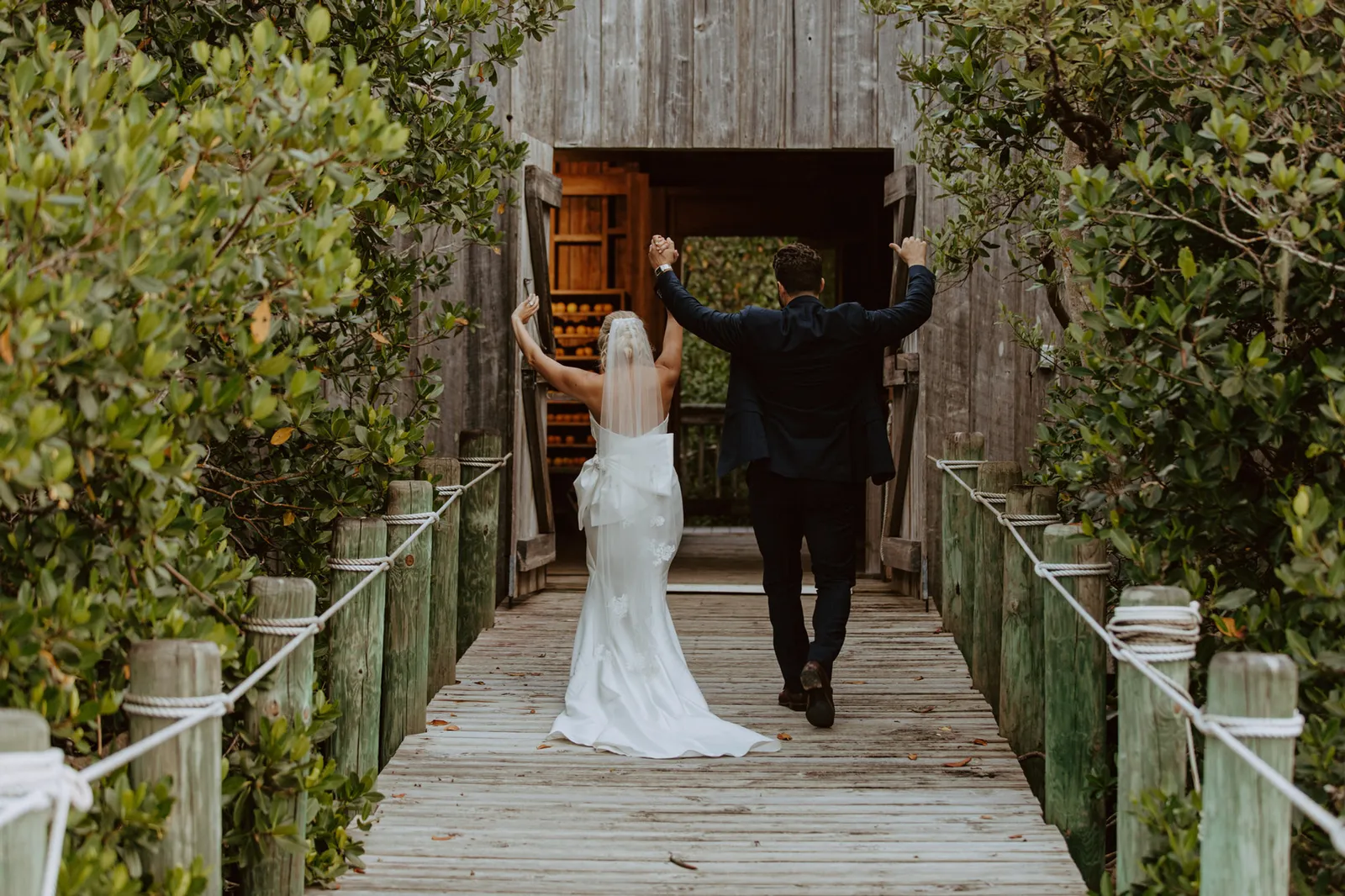 Newlyweds walking down a boardwalk with their arms raised