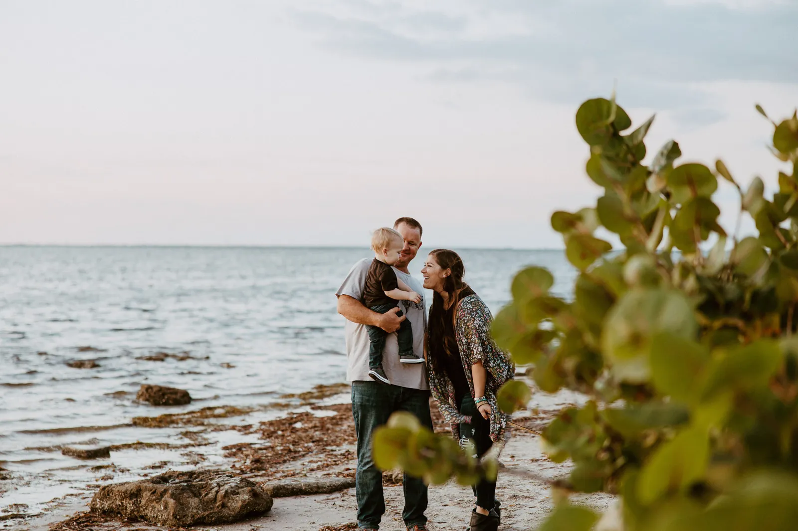 Parents kissing their son on the shore, framed by sea grape leaves