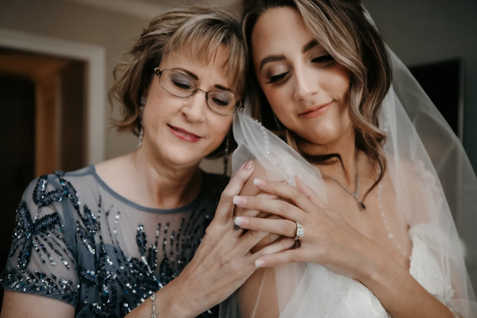 Bride and a woman in a beaded navy dress leaning their heads together