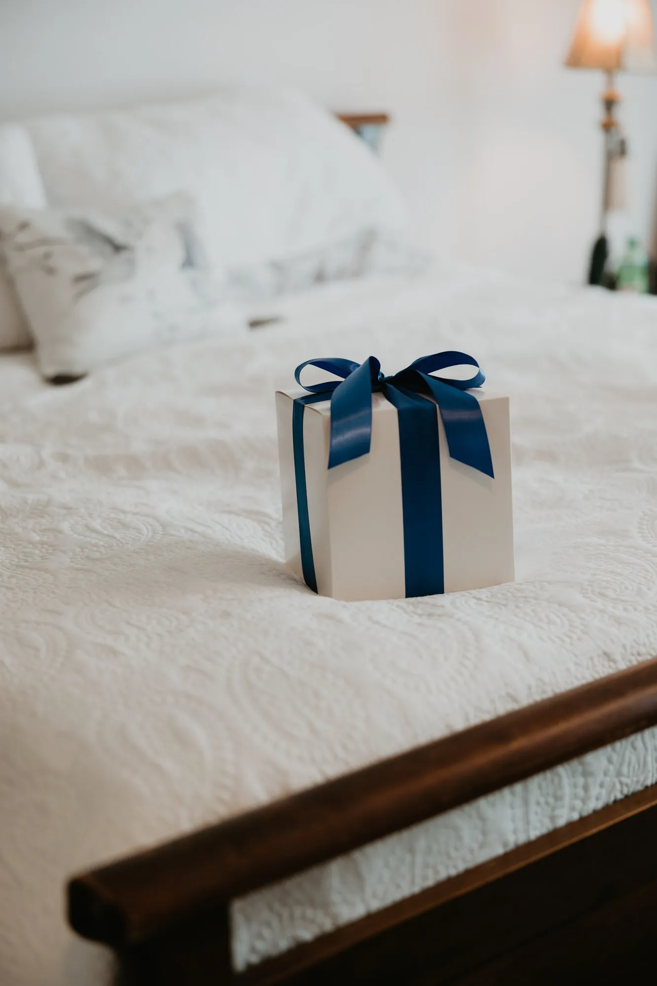 Gift box tied with a navy ribbon on a white bed