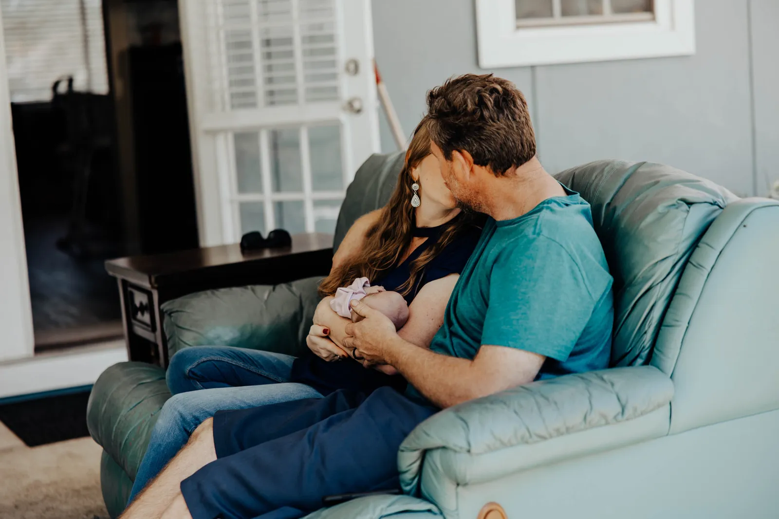 Parents kissing on a couch with their newborn between them