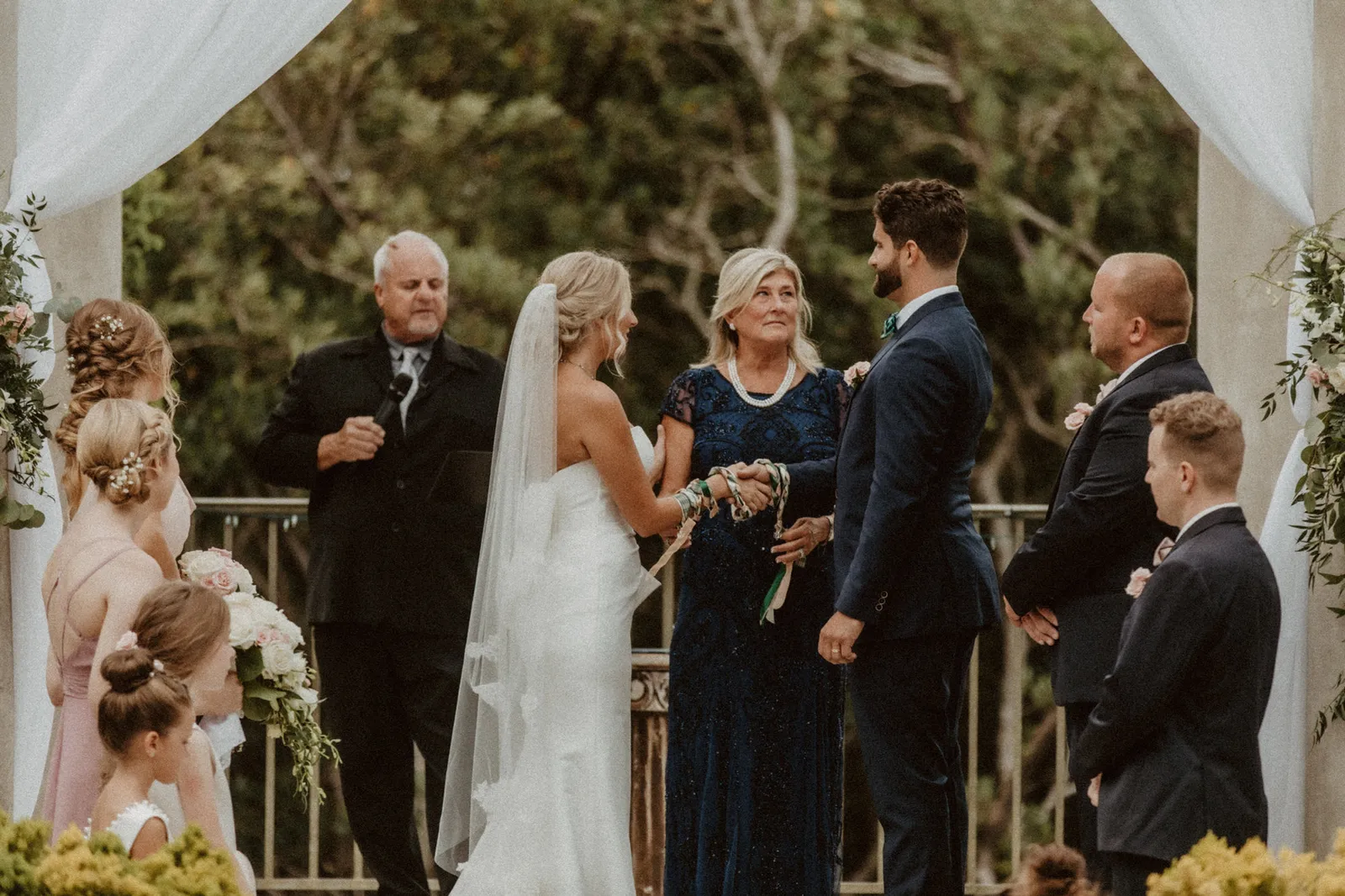 Wedding ceremony beneath a white draped arbor