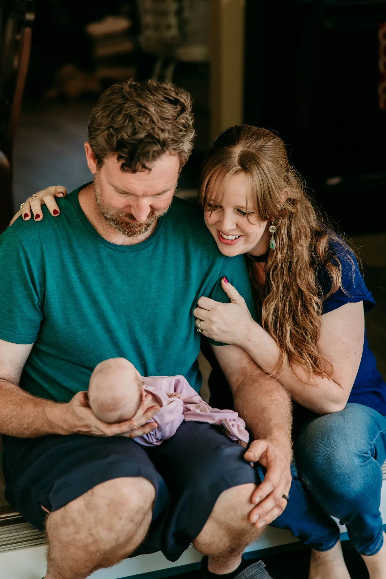 Father cradling the newborn on his lap as the mother leans on his shoulder, laughing
