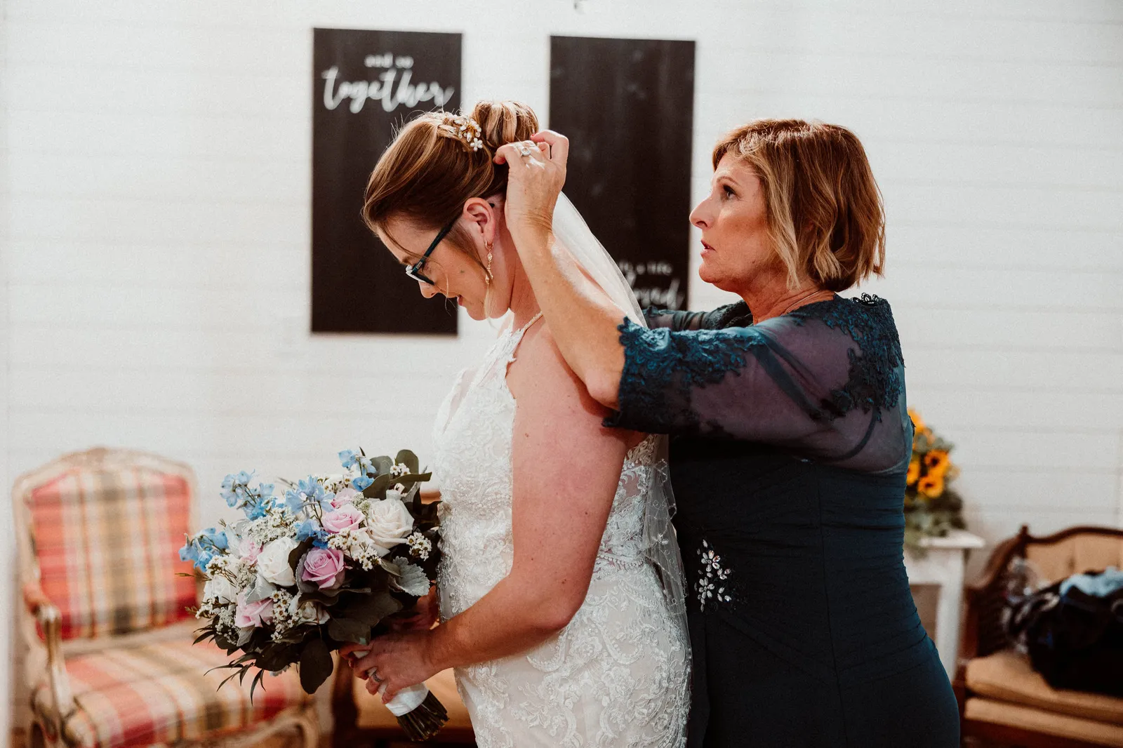 Woman in a navy lace dress fixing the bride's veil