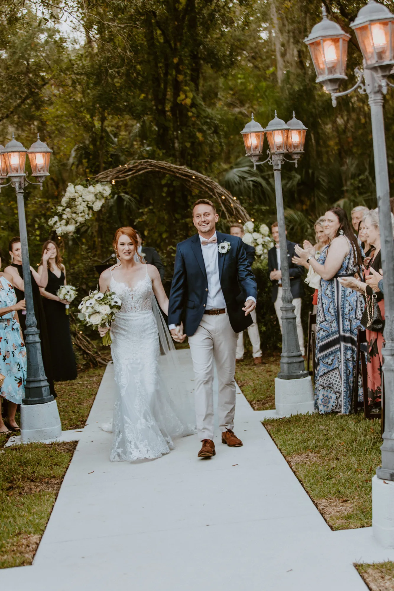 Newly married couple walking back up the aisle past lamp posts as guests cheer