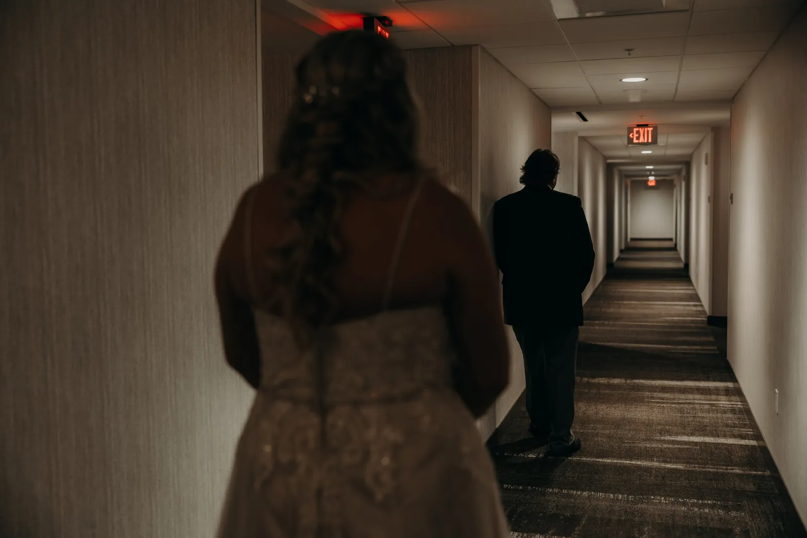 Bride watching from behind as a man walks ahead down the hotel corridor