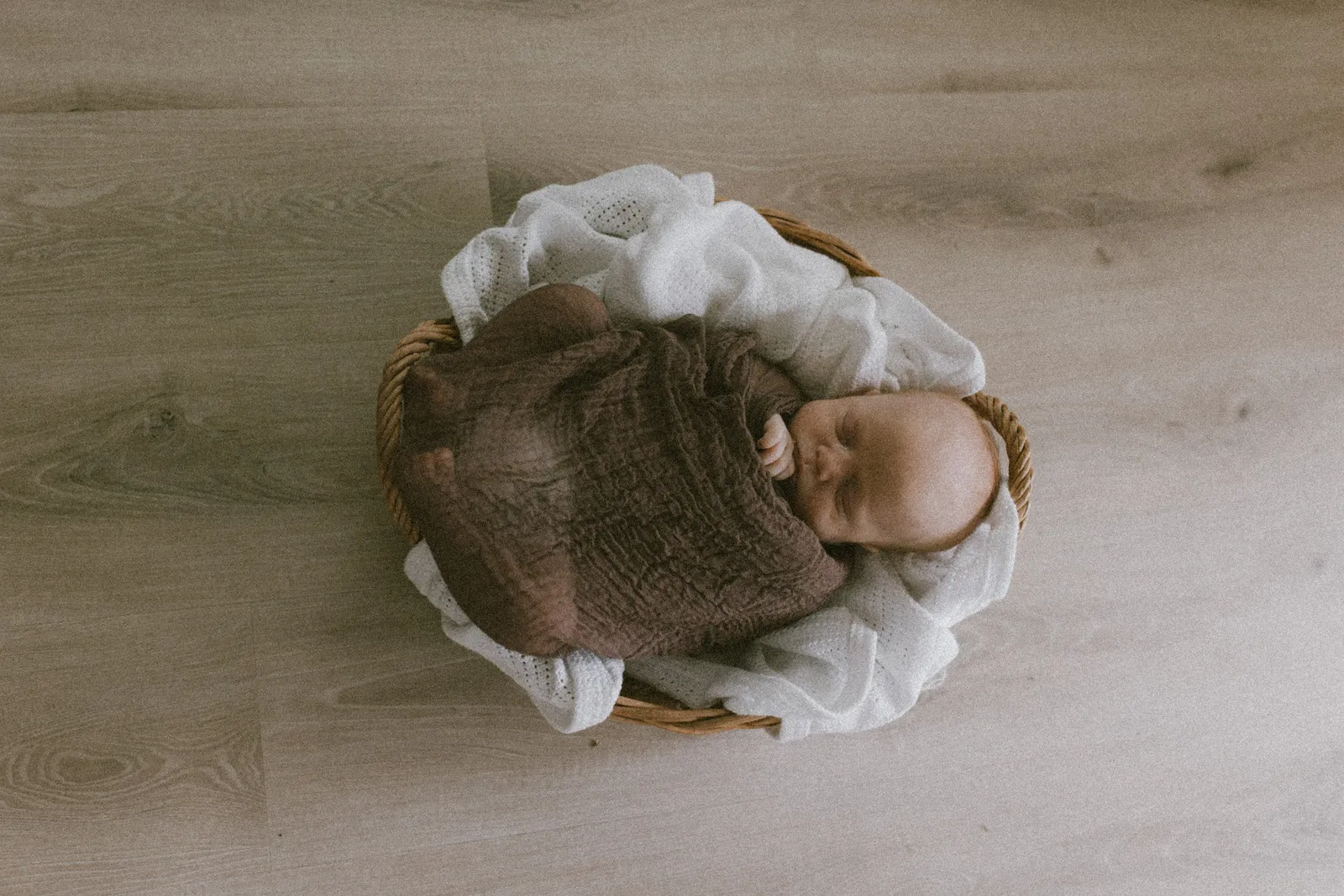 Newborn asleep in a basket, wrapped in brown muslin, seen from above