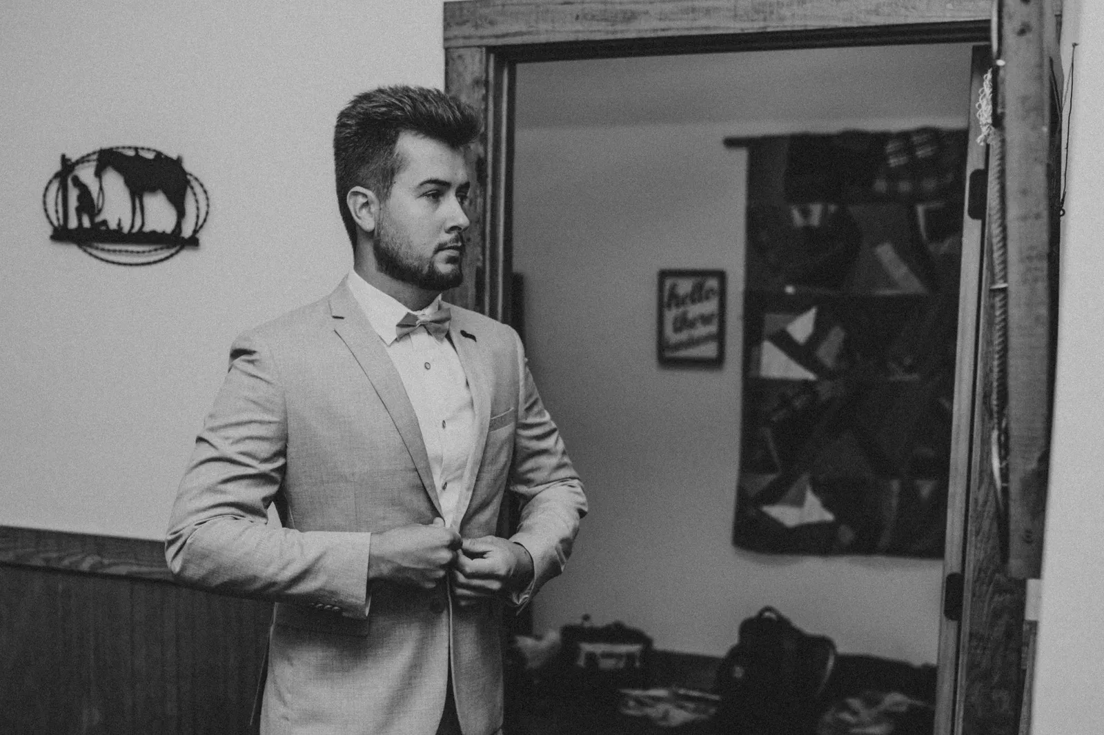 Groom in a grey suit buttoning his jacket, in black and white