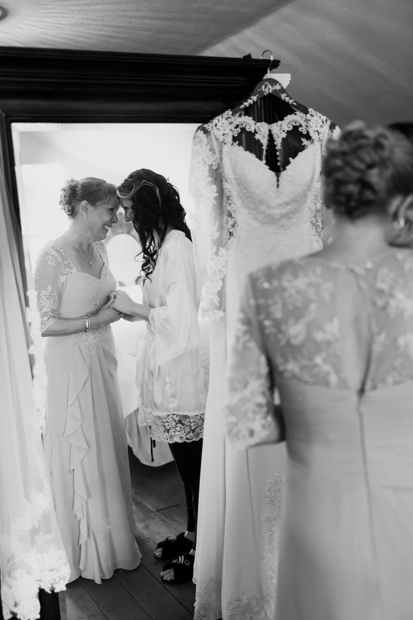 Bride and a woman in a long dress touching foreheads, in black and white