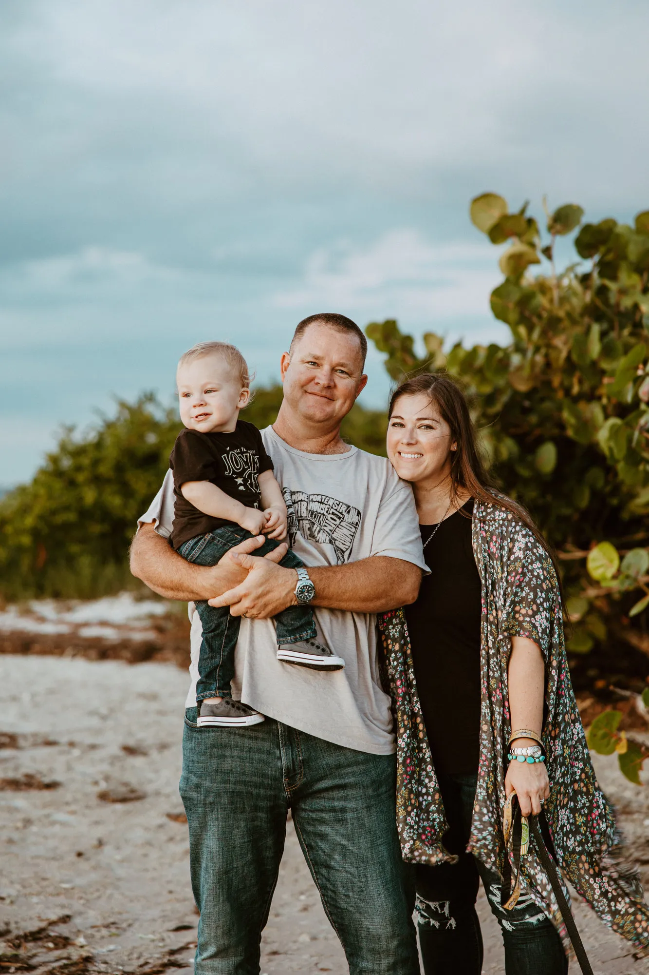 Family smiling together on the beach beside a sea grape tree