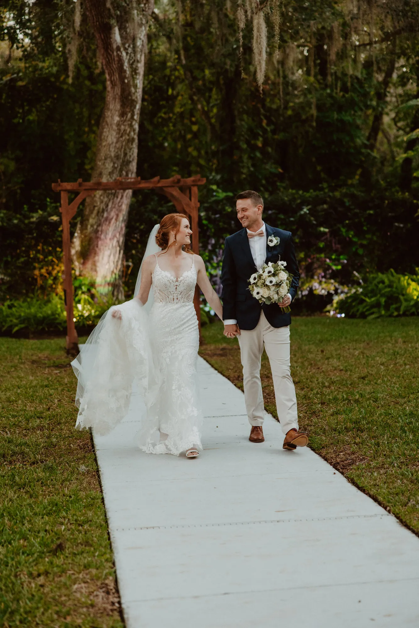 Bride and groom walking hand in hand down the path from a wooden arbor