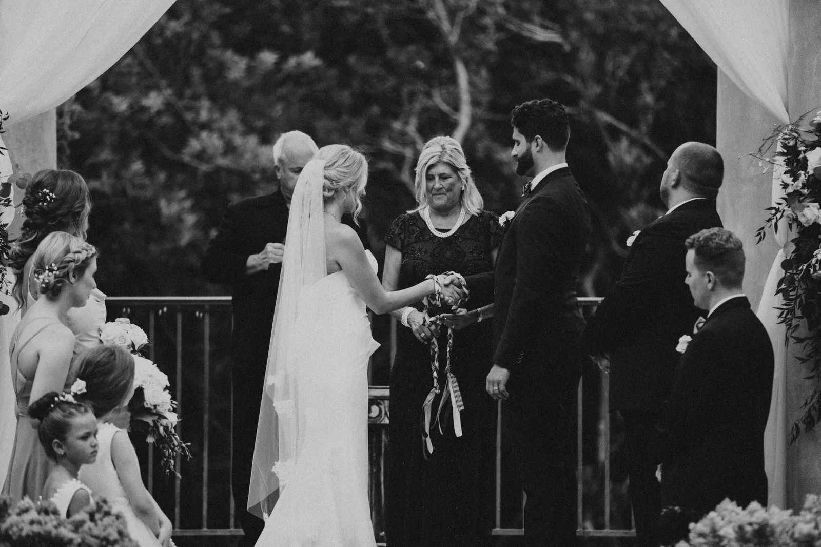 Woman tying a ribbon around the couple's joined hands during the ceremony, in black and white