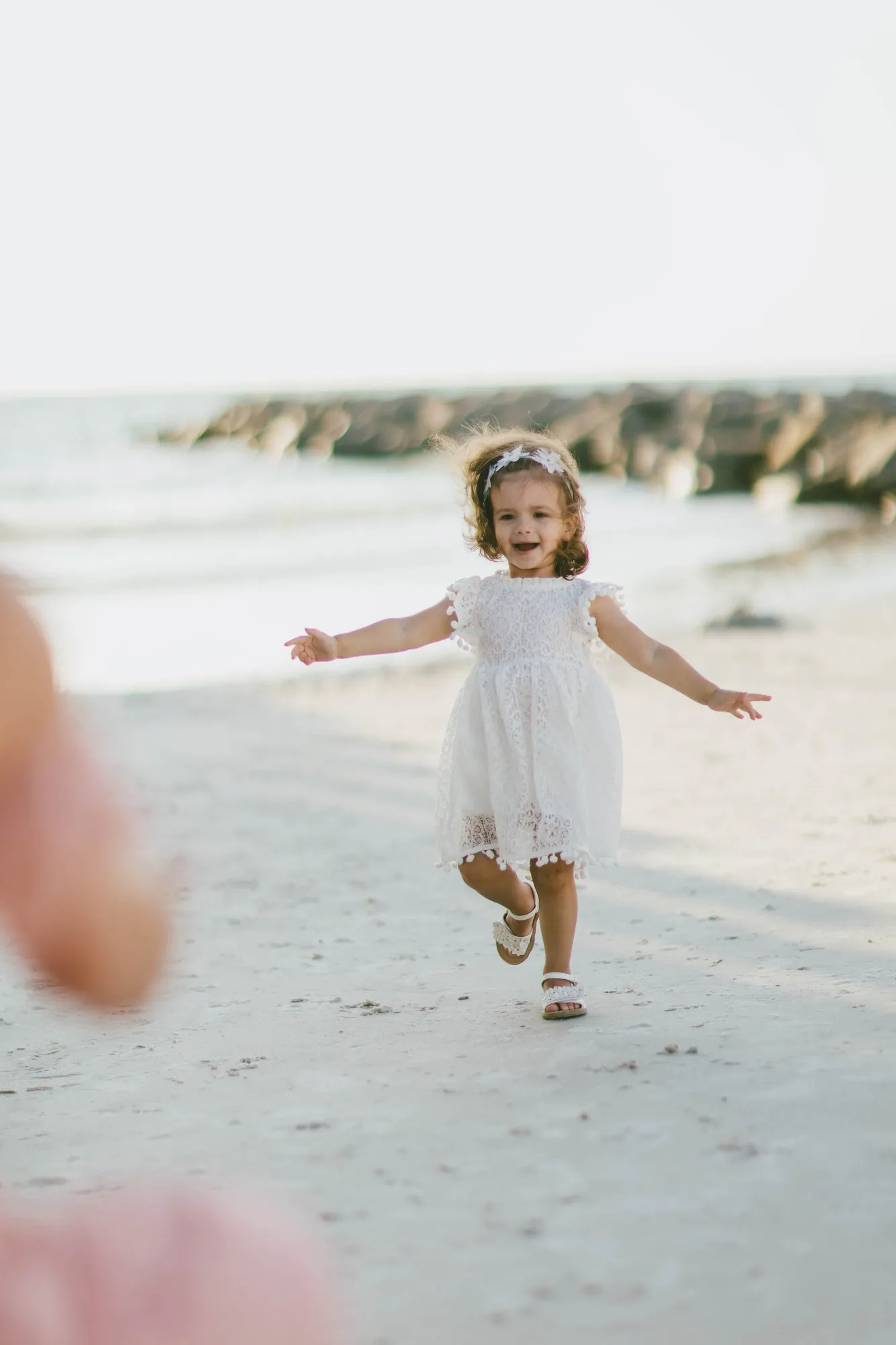 Toddler in a white dress running across the sand