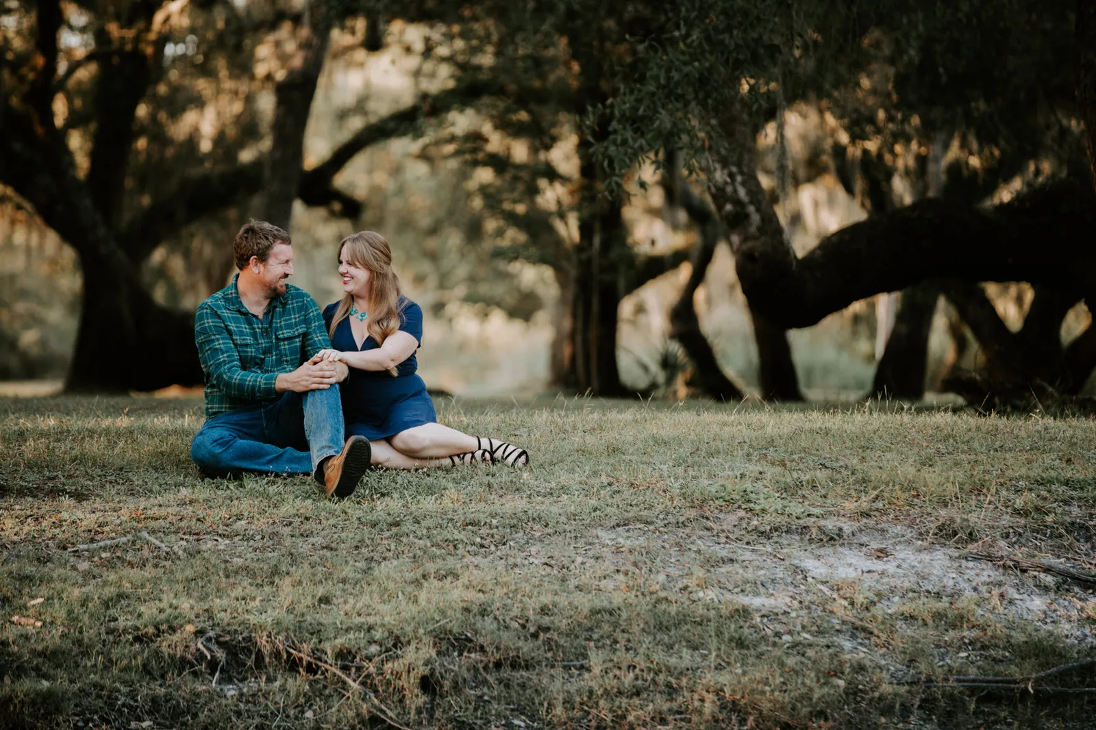 Couple sitting together on the grass under oak trees