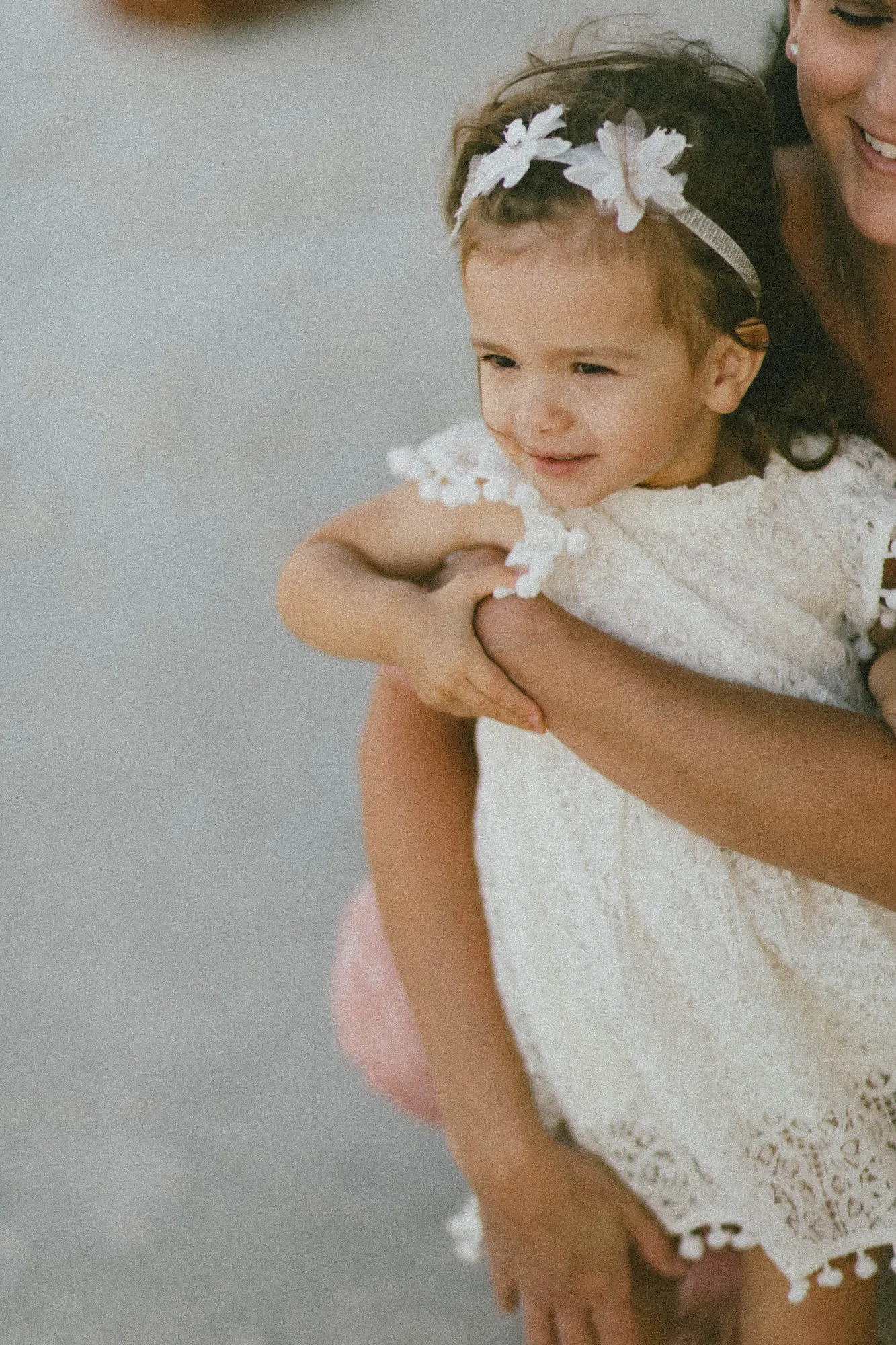 Toddler in a white lace dress held in her mother's arms